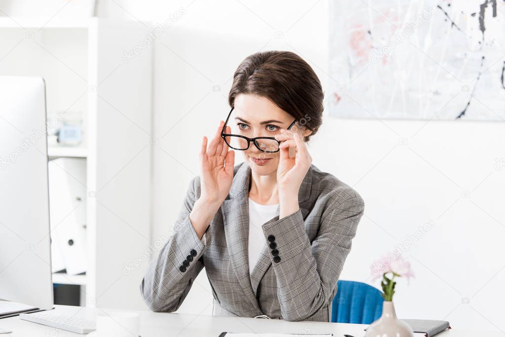 Attractive businesswoman in grey suit looking above glasses in office