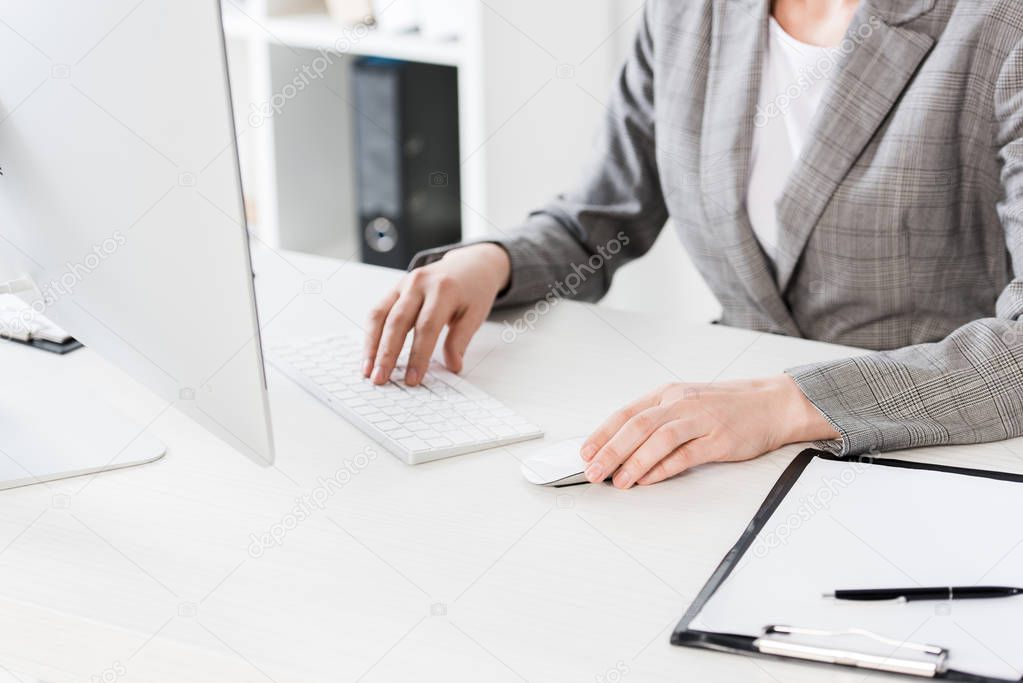 cropped image of businesswoman in grey suit sitting using computer in office