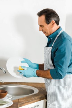 handsome mature man washing dishes in kitchen clipart