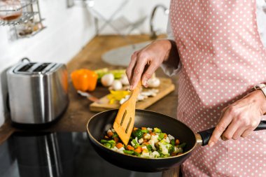 cropped image of mature woman frying vegetables in kitchen clipart