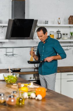 selective focus of handsome mature man cooking vegetables in kitchen clipart