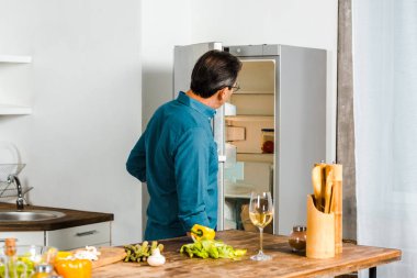 rear view of mature man looking into open fridge in kitchen clipart