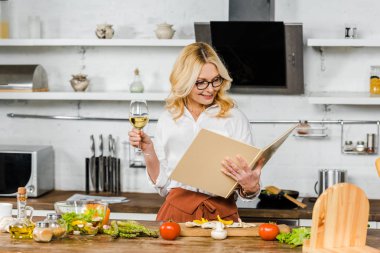 şarap tutarak ve mutfak yemek kitabı bakarak çekici Olgun kadın