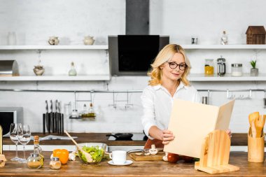 çekici Olgun kadın mutfakta yemek tarifi kitabı alarak