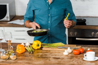 cropped image of middle aged man cooking vegetables on frying pan in kitchen clipart