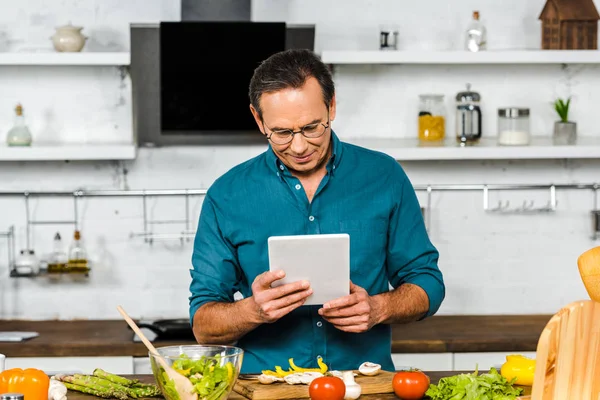 Guapo Hombre Maduro Usando Tableta Mientras Cocina Cocina —  Fotos de Stock