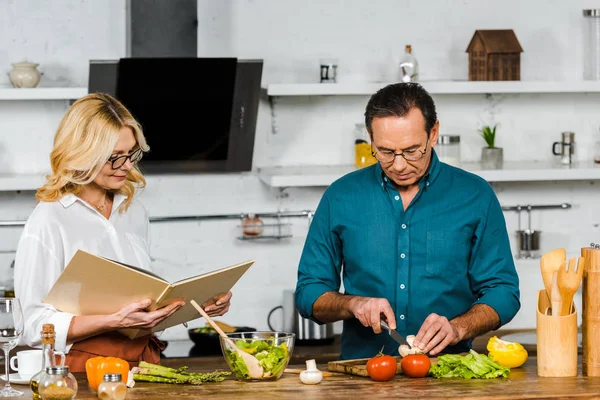 中年妻子和丈夫一起烹饪食谱书在厨房 — 图库照片