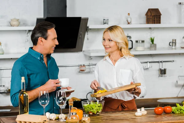 Smiling Attractive Mature Wife Putting Vegetables Bowl Husband Holding Cup — Stock Photo, Image