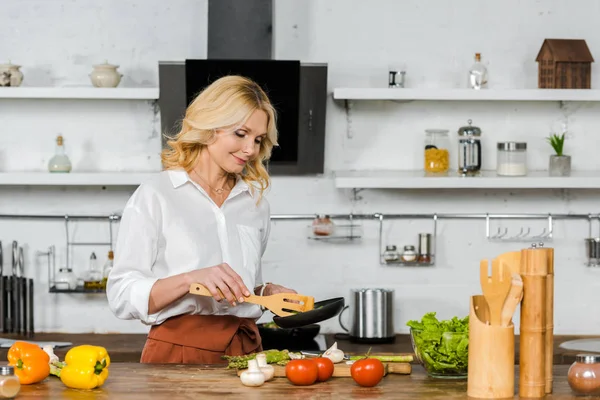 魅力的な中年の女性の台所でフライパンで野菜を調理 — ストック写真