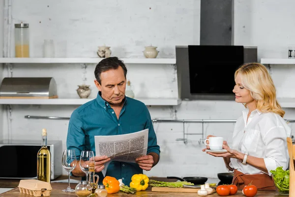 Esposa Madura Sosteniendo Taza Marido Leyendo Periódico Mientras Cocina Cocina — Foto de Stock