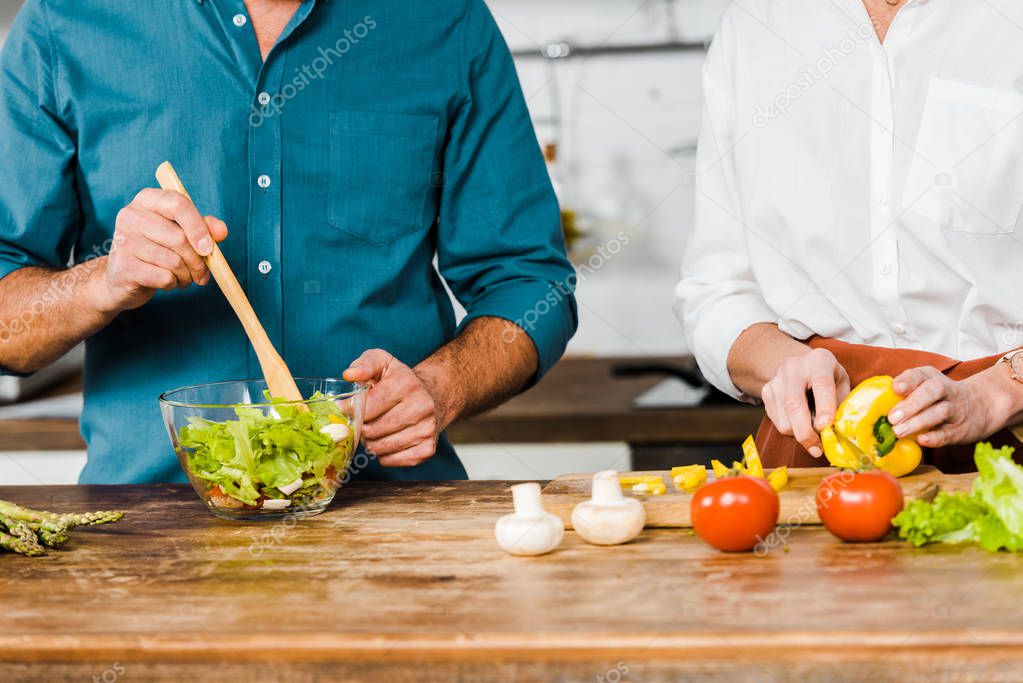 cropped image of mature wife and husband cooking salad together in kitchen