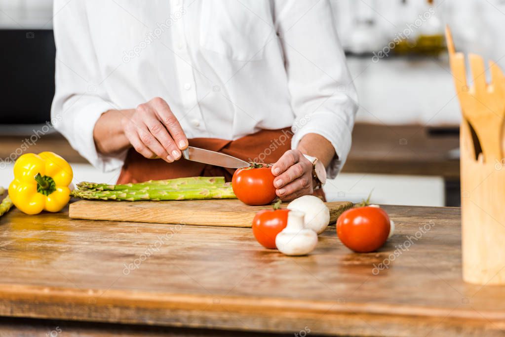 cropped image of middle aged woman cutting vegetables in kitchen