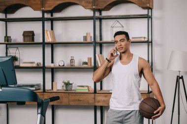  oturma odasında basketbol tutarken Smartphone'da konuşan karışık yarış adam 