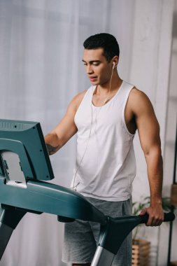  mixed race man listening music in earphones and exercising on treadmill 