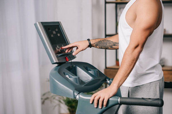 cropped view of sportsman pushing sensor button on control panel of  treadmill 