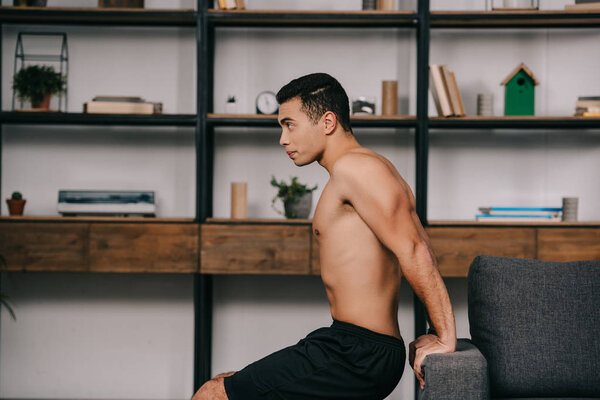 handsome mixed race man exercising near sofa in living room 