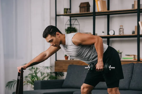 handsome bi-racial man holding chair and doing exercise with dumbbell