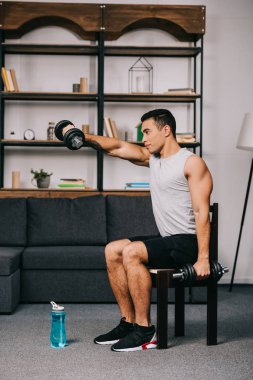 yakışıklı karışık yarış adam sandalyede otururken ağır dumbbells holding