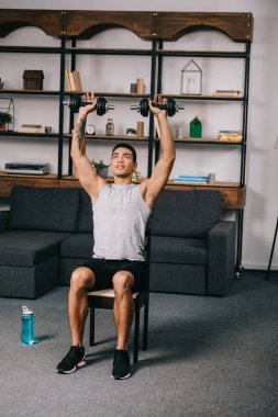 ağır dumbbells sandalyede oturma odasında otururken üzerinde kafa tutan karışık yarış atlet