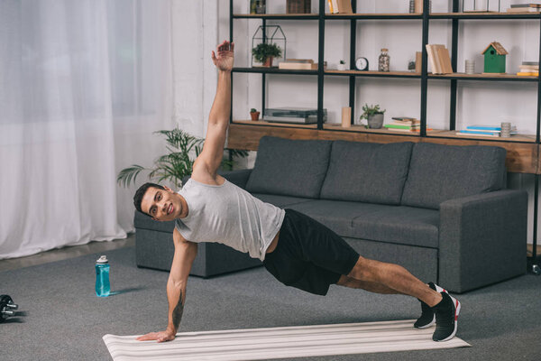 bi-racial man doing plank exercise on fitness mat in living room 