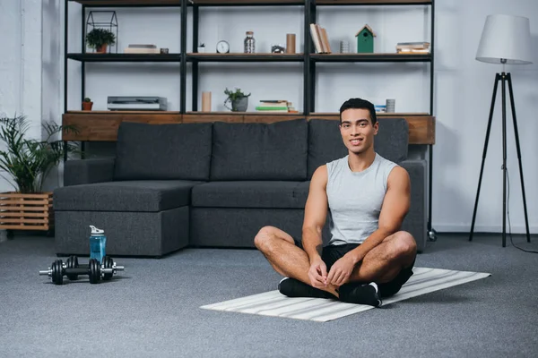 在客厅里坐在健身垫上的开朗的双种族男子 — 图库照片
