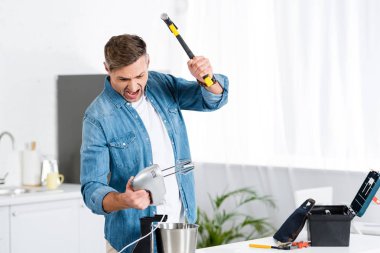 angry adult man screaming and holding mixer and hammer 