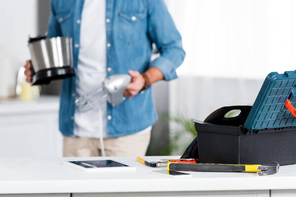 selective focus of tool box and hammer on table and man holding mixer on background 