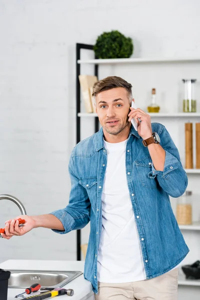 Confused Handsome Man Talking Smartphone While Holding Repair Tool — Stock Photo, Image