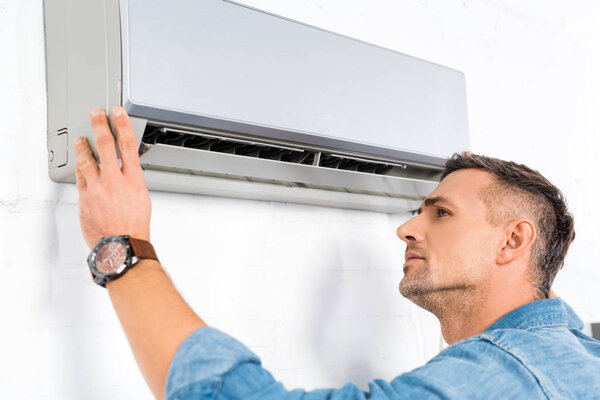 handsome adult man looking into air conditioner  