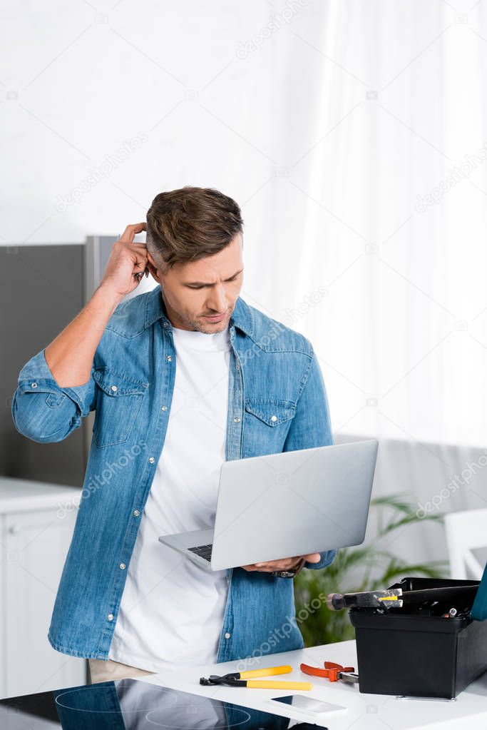 confused man holding laptop with tool box on table in kitchen 