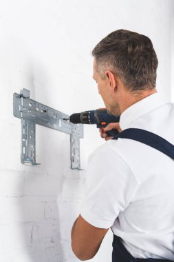 rear view of adult man installing bracket for air conditioner with drill clipart