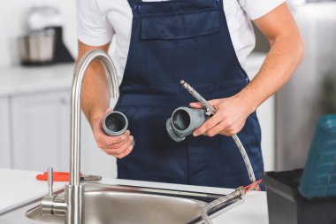 cropped view of repairman holding pipes and tools while repairing faucet at kitchen  clipart