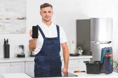 Mutfak ayakta ve kameraya bakarak süre yetişkin tamirci gösteren smartphone gülümseyen 