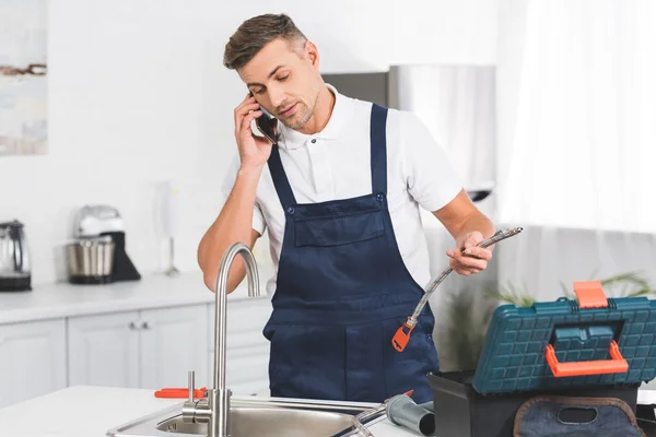 Adult Repairman Holding Pipe Talking Smartphone While Repairing Kitchen Faucet — Stock Photo, Image