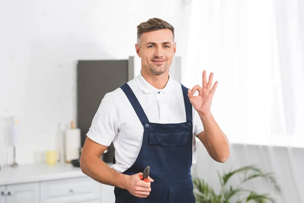 Sonriente Reparador Adulto Sosteniendo Alicates Mientras Muestra Signo Mirando Cámara — Foto de Stock