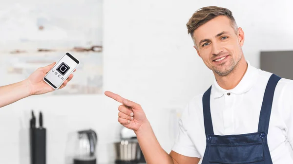 Partial View Hand Holding Smartphone Smiling Adult Repairman Pointing Finger — Stock Photo, Image