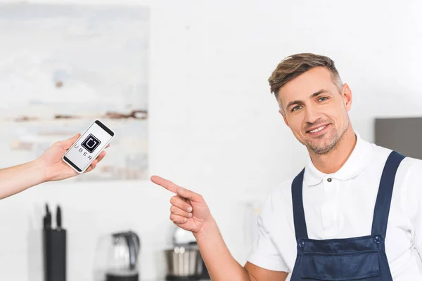 Partial View Hand Holding Smartphone Smiling Adult Repairman Pointing Finger — Stock Photo, Image