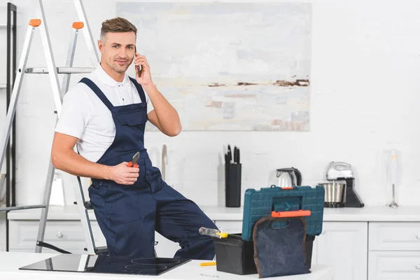 Glimlachend Volwassen Reparateur Zittend Ladder Holding Tangen Praten Door Smartphone — Stockfoto