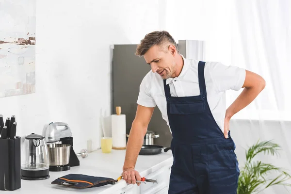 Thoughtful Adult Repairman Holding Pliers While Leaning Kitchen Counter — Stock Photo, Image