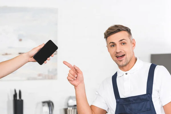 Partial View Hand Holding Smartphone Smiling Adult Repairman Pointing Blank — Stock Photo, Image