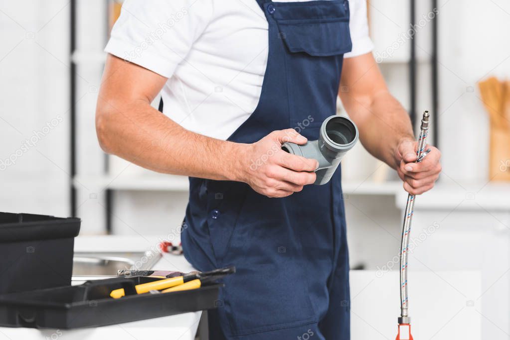 cropped view of repairman holding pipes for repairing kitchen faucet