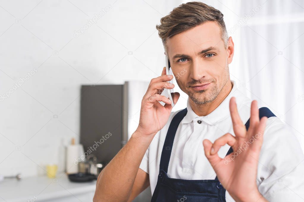 adult repairman talking on smartphone and showing ok sign