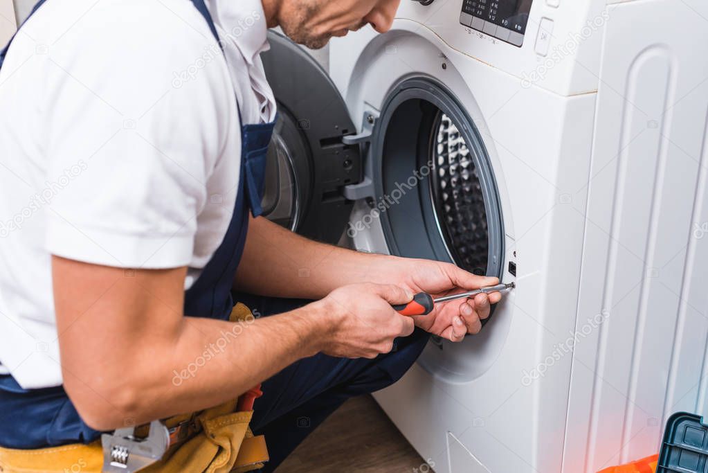 cropped view of adult repairman working with screwdriver while repairing washing machine in bathroom 