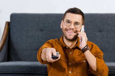 seçici odak neşeli adam uzaktan kumanda holding ve Smartphone'da konuşuyor