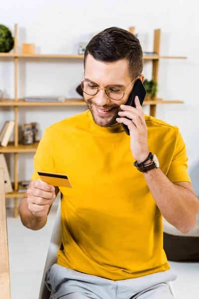 Hombre Sonriente Gafas Mirando Tarjeta Crédito Mientras Habla Teléfono Inteligente — Foto de Stock