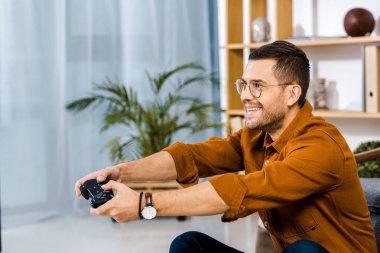 happy man in glasses playing video game at home clipart