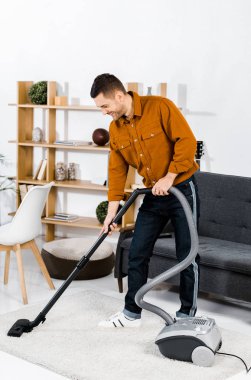 gülümseyen ve hoover ile temizlik modern oturma odasında yakışıklı adam 