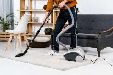 cropped view of man in modern living room cleaning house with hoover  clipart