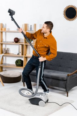 gülümseyen ve hoover kadar yükselen modern oturma odasında yakışıklı adam 