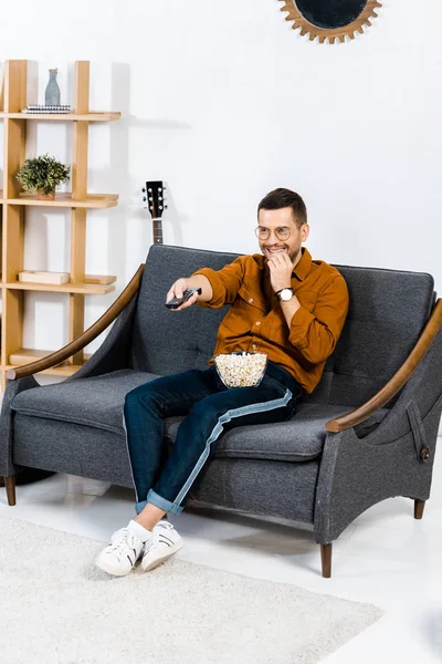 Homem Alegre Sentado Sofá Segurando Controle Remoto Comendo Pipocas — Fotografia de Stock